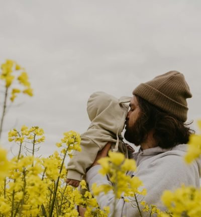 Parents-4 a man kissing a baby in a field of yellow flowers